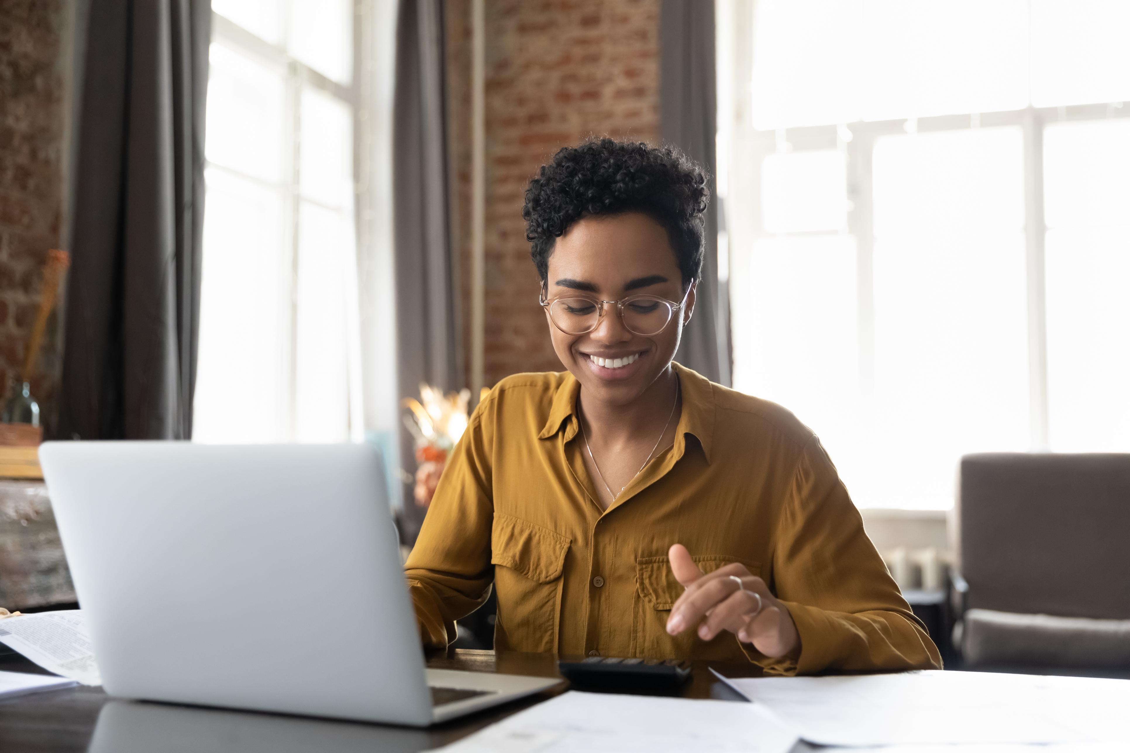 A smiling woman focused on her laptop, engaged in work with a positive demeanor.